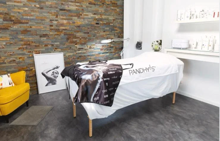 Behandlungsraum mit Liege, Steinwand und gelbem Sessel